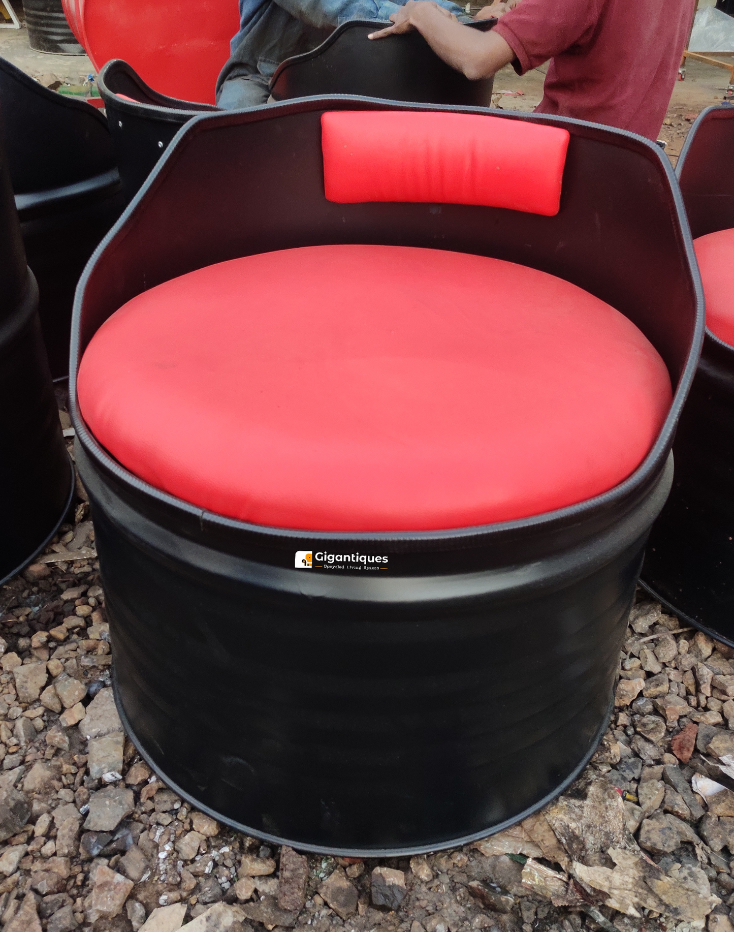 Eco-friendly low back curve shape chair by Gigantiques made from upcycled metal drum, featuring a vibrant red cushion.